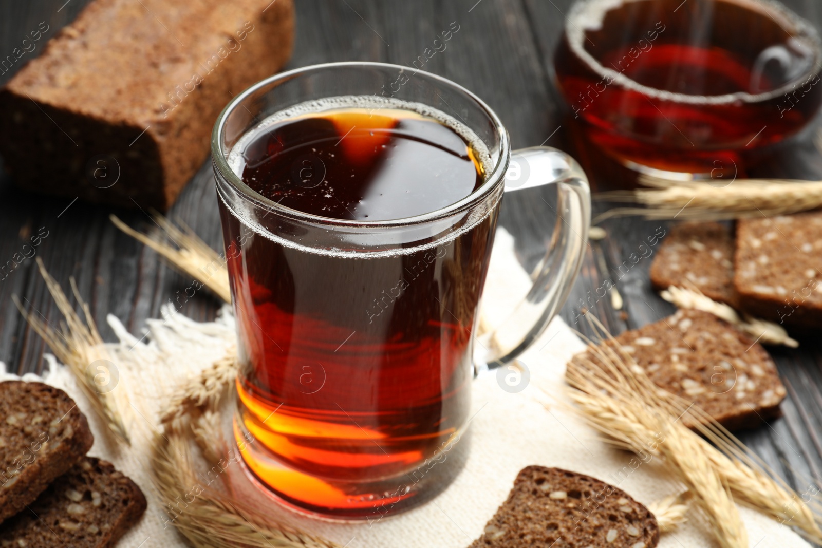 Photo of Mug of delicious kvass, spikes and bread on table