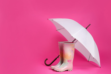 Photo of Beautiful white umbrella and colorful rubber boots on pink background. Space for text