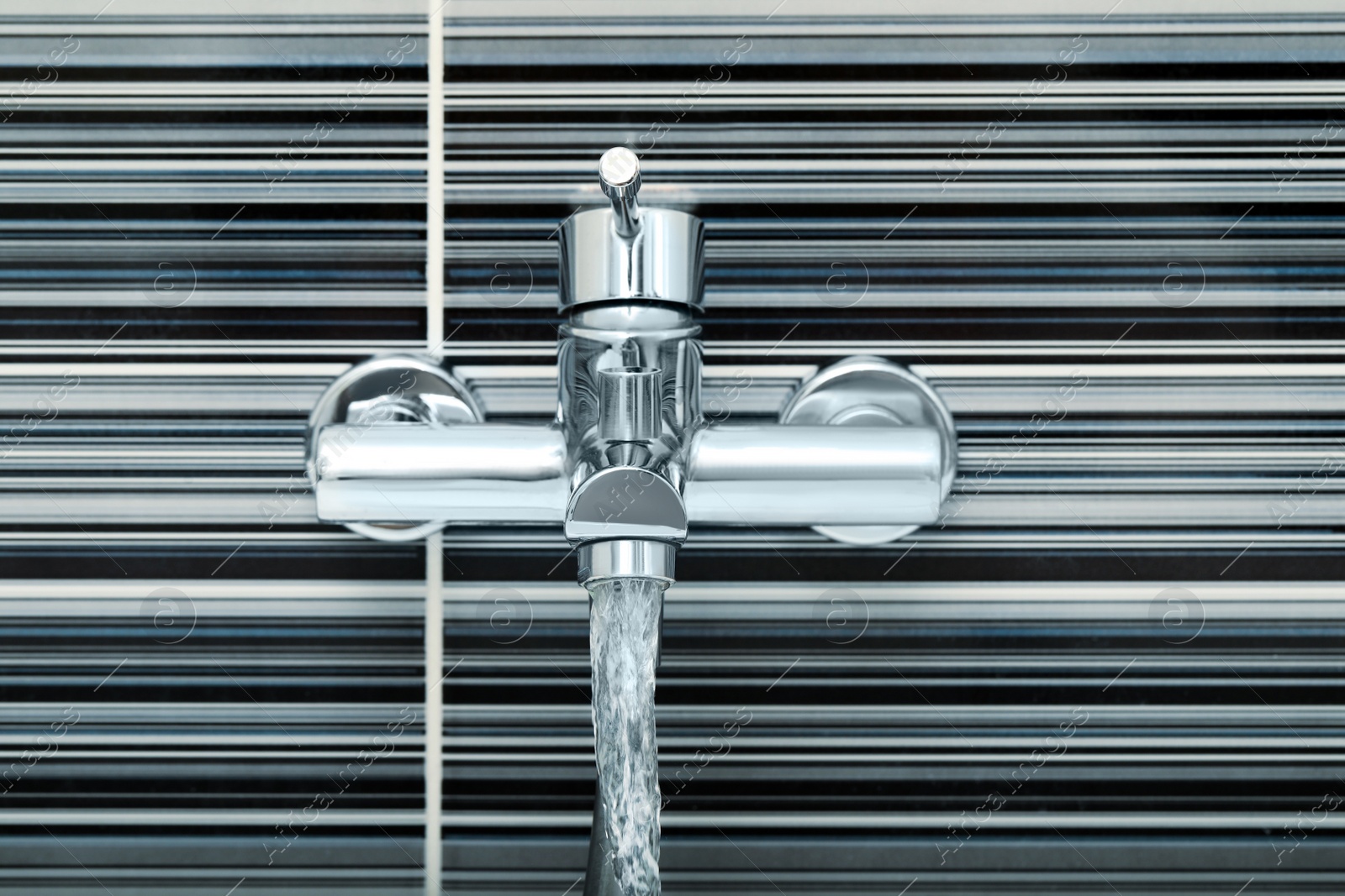 Photo of Water flowing from bath tap installed on black and white wall