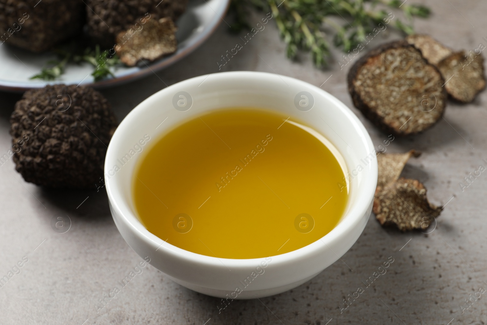 Photo of Fresh truffles and oil in bowl on light grey table, closeup