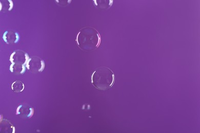 Beautiful transparent soap bubbles on violet background, space for text