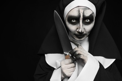 Photo of Scary devilish nun with knife on black background, space for text. Halloween party look