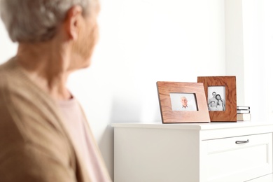 Elderly woman looking at framed family portraits indoors