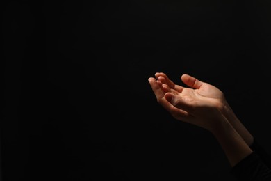 Religion. Woman with open palms praying on black background, closeup. Space for text