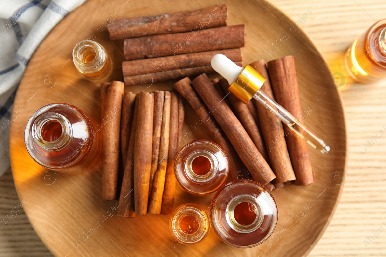 Photo of Bottles of essential oils and cinnamon sticks on wooden plate, top view