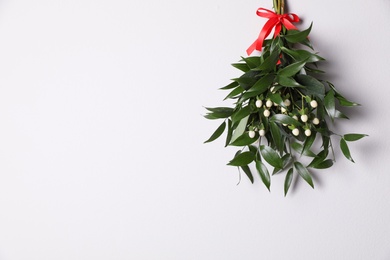 Mistletoe bunch with red bow hanging on white wall, space for text. Traditional Christmas decor