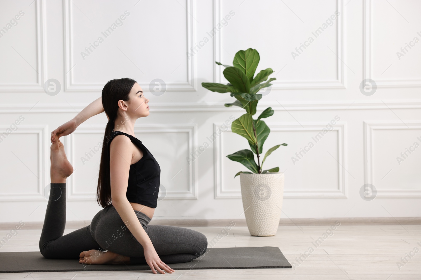 Photo of GIrl practicing one legged king pigeon asana on mat in yoga studio. Eka pada rajakapotasana pose