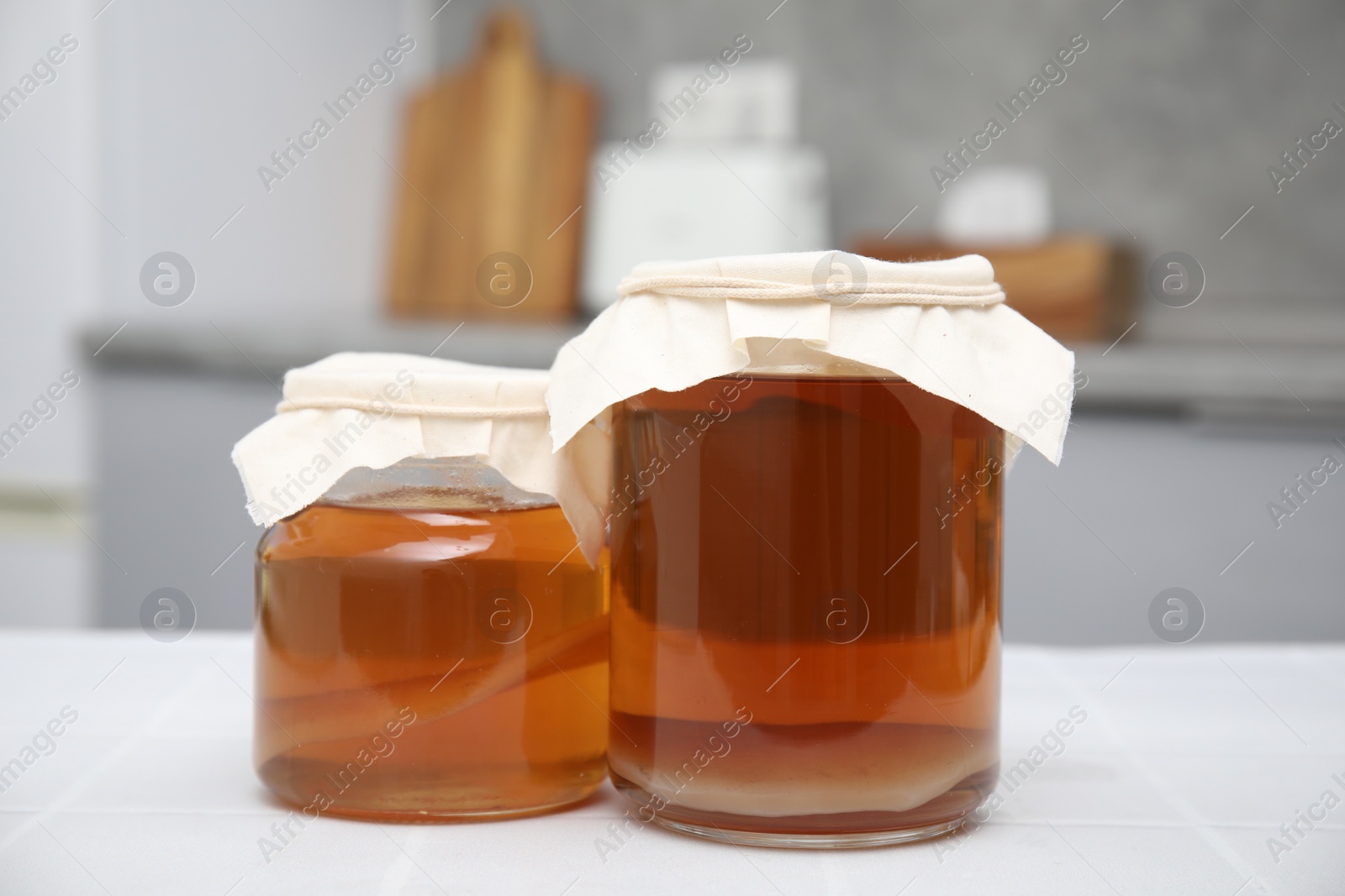 Photo of Homemade fermented kombucha in glass jars on white table in kitchen