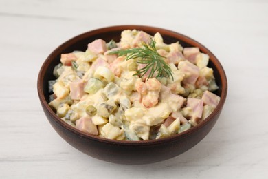 Photo of Tasty Olivier salad with boiled sausage in bowl on white wooden table