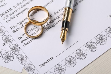 Photo of Marriage contract, gold rings and pen on light wooden table, top view