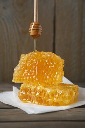 Dripping tasty honey from dipper onto honeycombs on wooden table