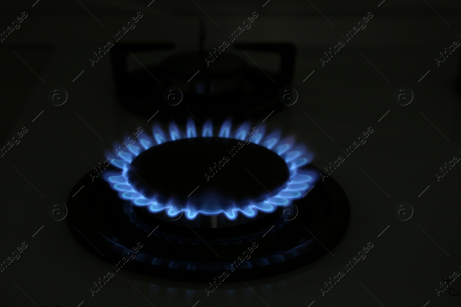 Photo of Modern gas cooktop with burning blue flame in kitchen at night