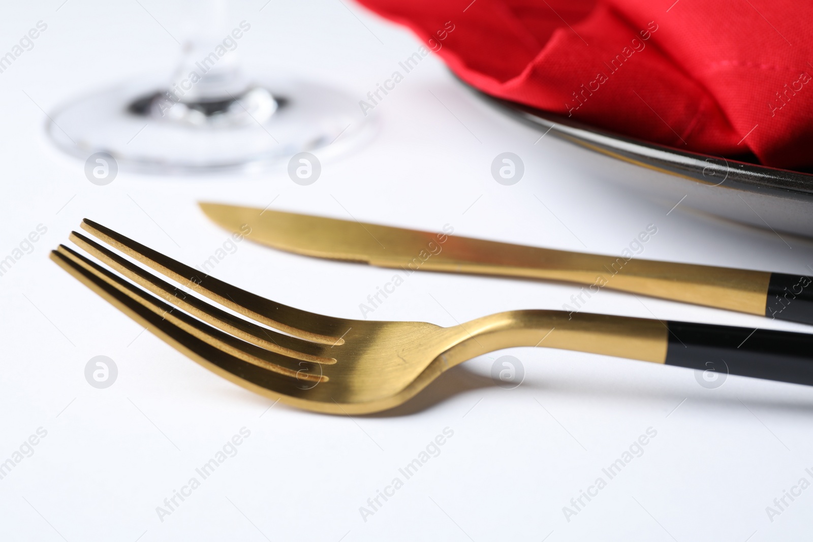Photo of Golden cutlery near plate on white table, closeup