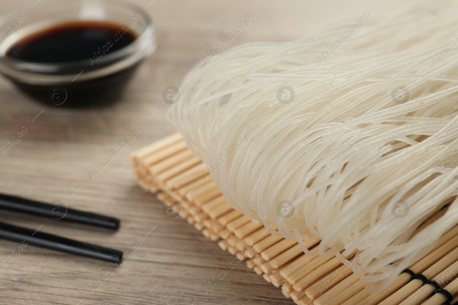 Photo of Dried rice noodles with chopsticks and soy sauce on wooden table, closeup