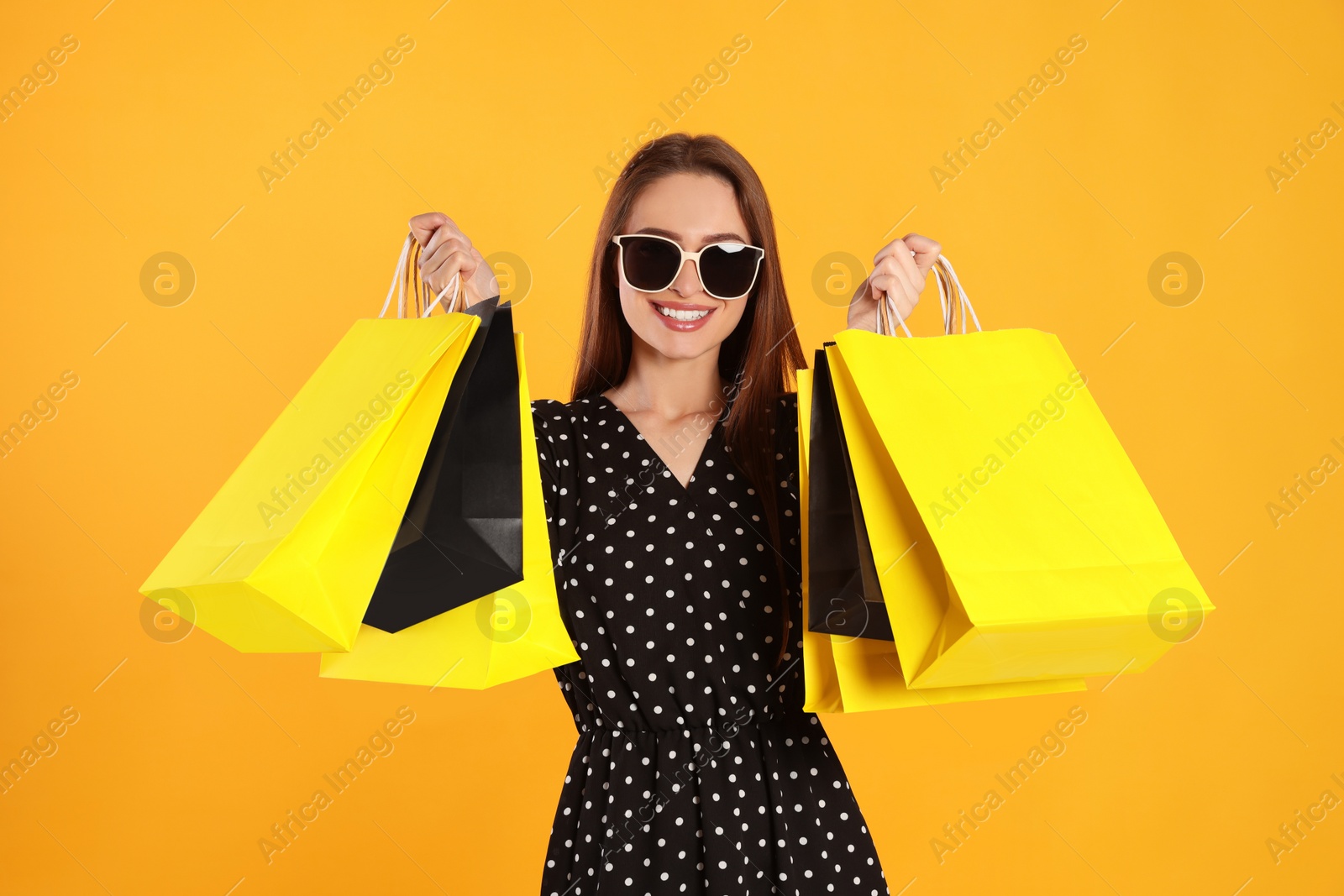 Photo of Happy young woman with shopping bags on yellow background. Big sale