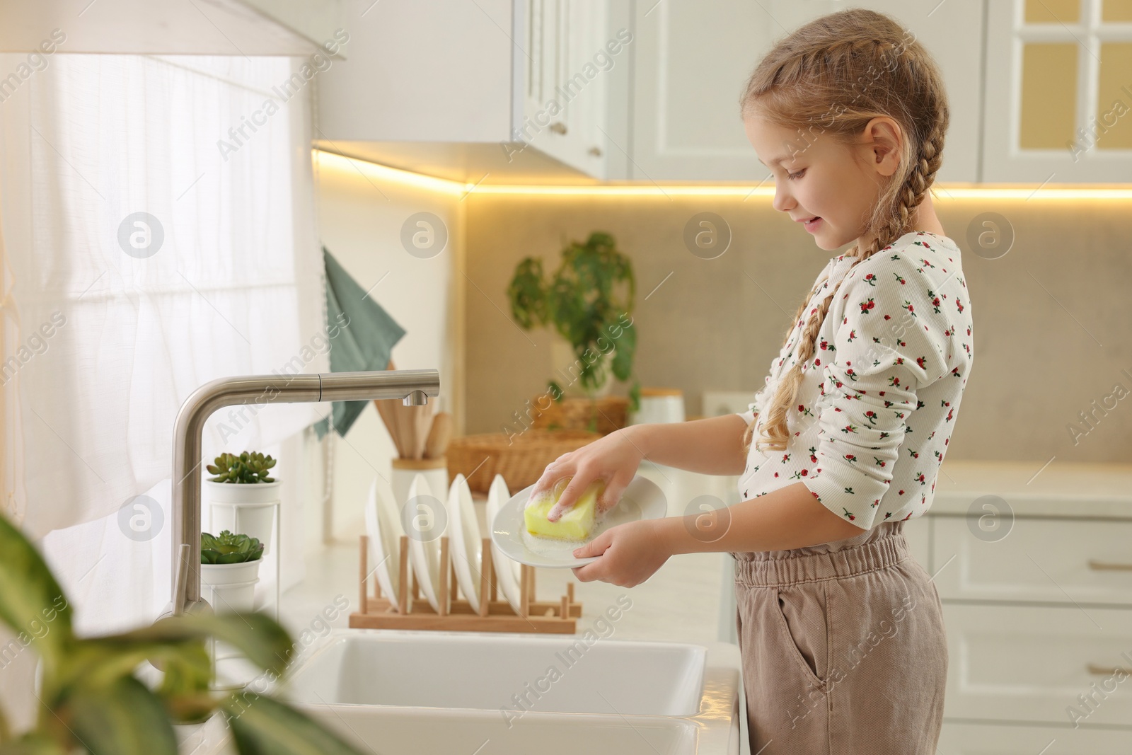 Photo of Little girl washing plate above sink in kitchen