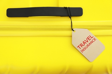 Photo of Yellow suitcase with TRAVEL INSURANCE label, top view