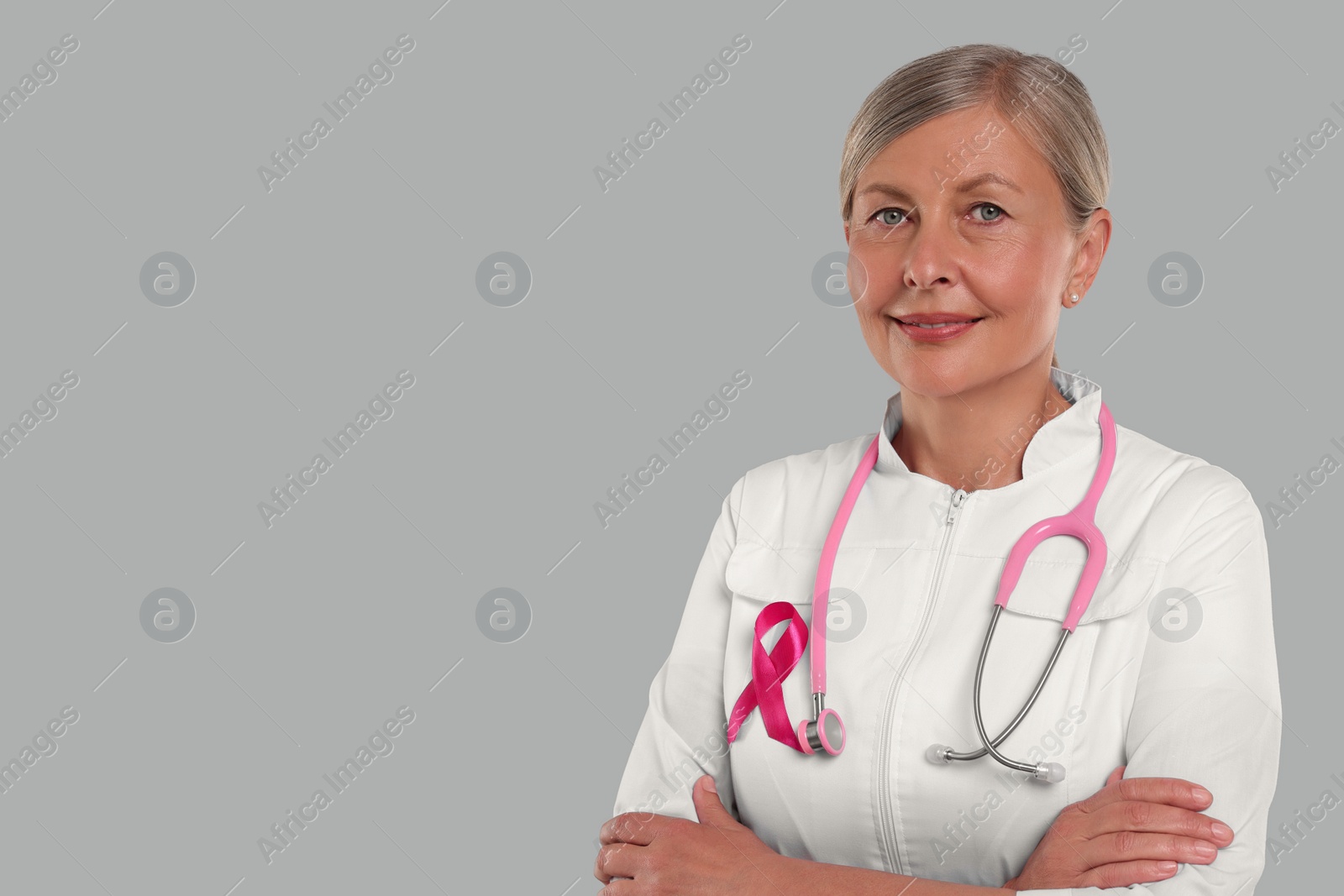 Photo of Doctor with pink ribbon and stethoscope on light grey background, space for text. Breast cancer awareness