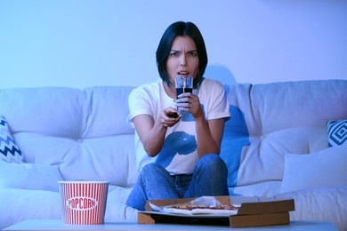 Emotional woman watching TV with popcorn and pizza on sofa