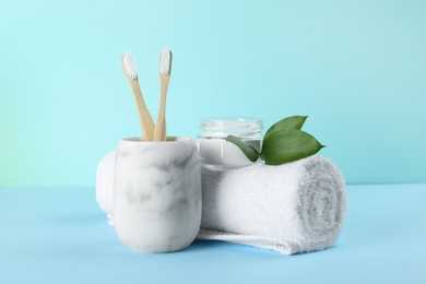 Bamboo toothbrushes, towel and bowl of baking soda on light blue background