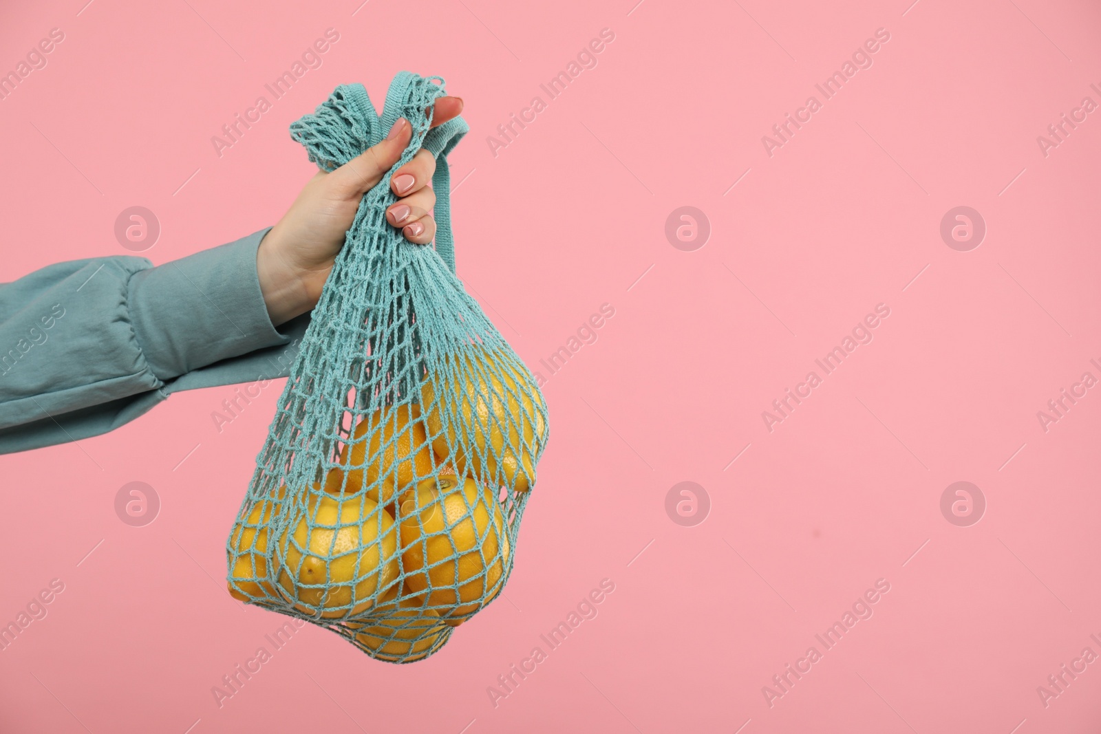 Photo of Woman with string bag of fresh lemons on pink background, closeup. Space for text