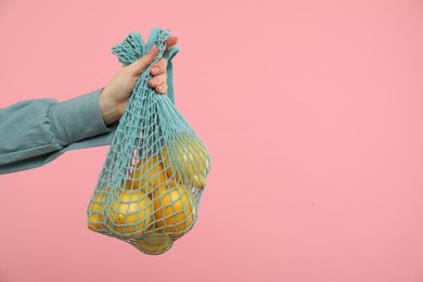 Woman with string bag of fresh lemons on pink background, closeup. Space for text