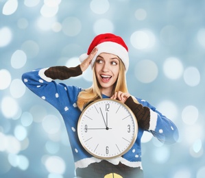 New Year countdown. Excited woman in Santa hat holding clock on light blue background