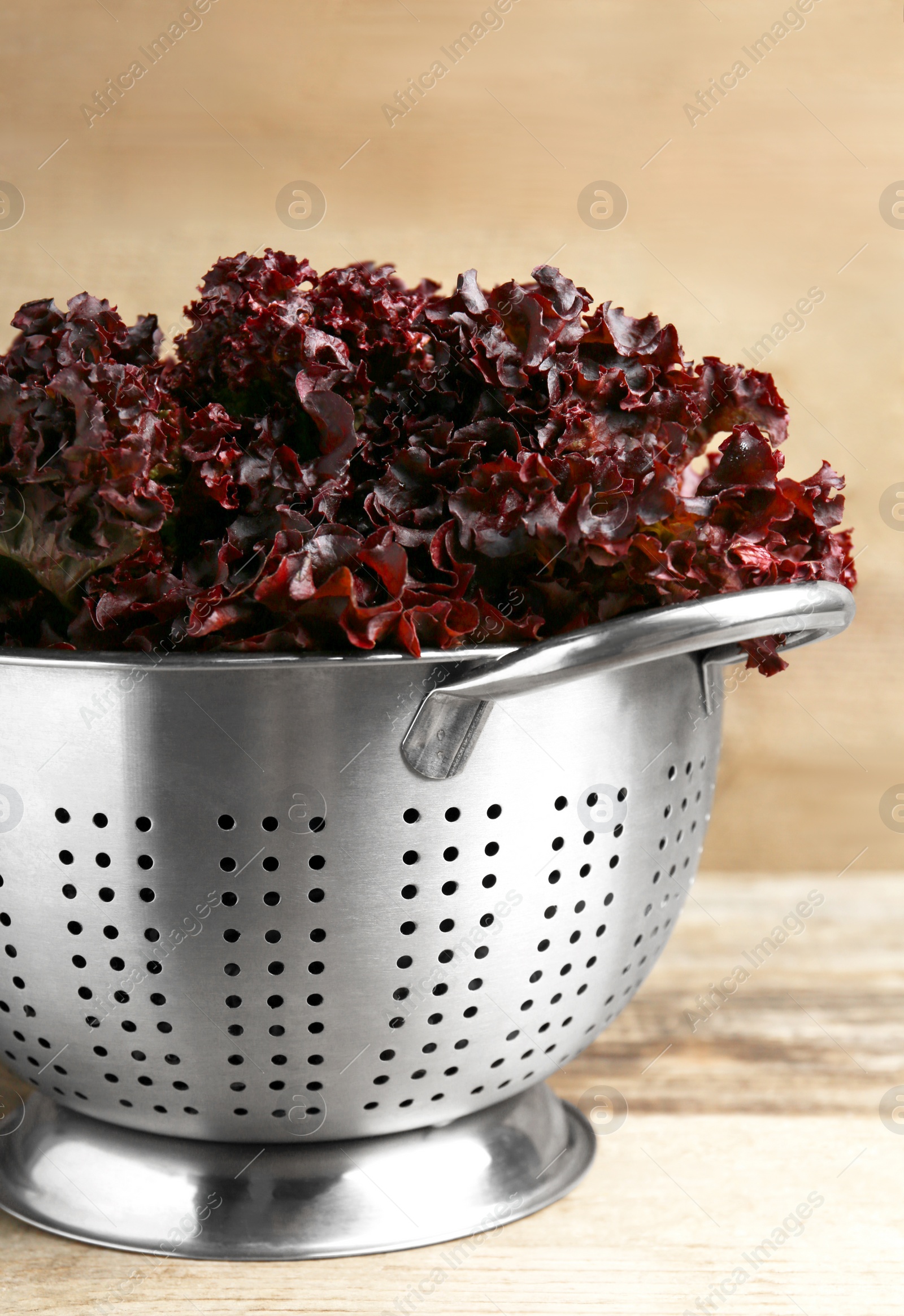 Photo of Colander with red coral lettuce on wooden table, closeup