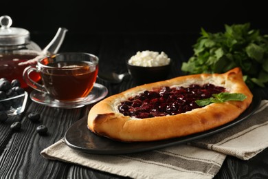 Photo of Delicious sweet cottage cheese pastry with cherry jam on black wooden table
