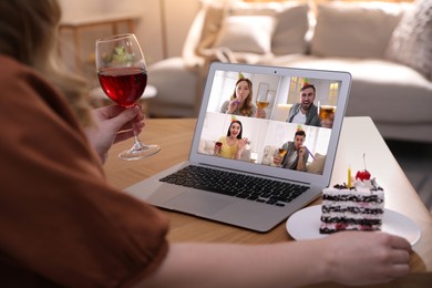 Woman with glass of wine and cake having online party via laptop at home during quarantine lockdown, closeup