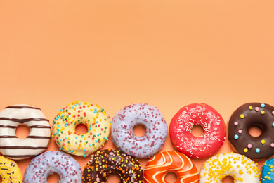 Photo of Delicious glazed donuts on orange background, flat lay. Space for text