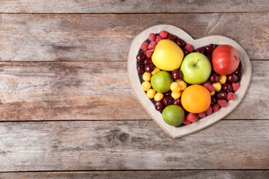 Photo of Heart shaped plate with fresh fruits on wooden table, top view. Cardiac diet