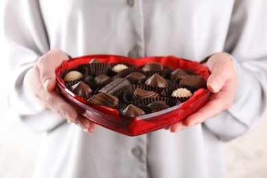 Woman holding heart shaped box with delicious chocolate candies, closeup