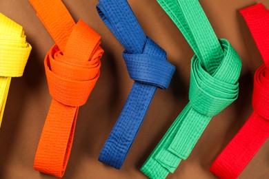 Photo of Colorful karate belts on brown background, flat lay