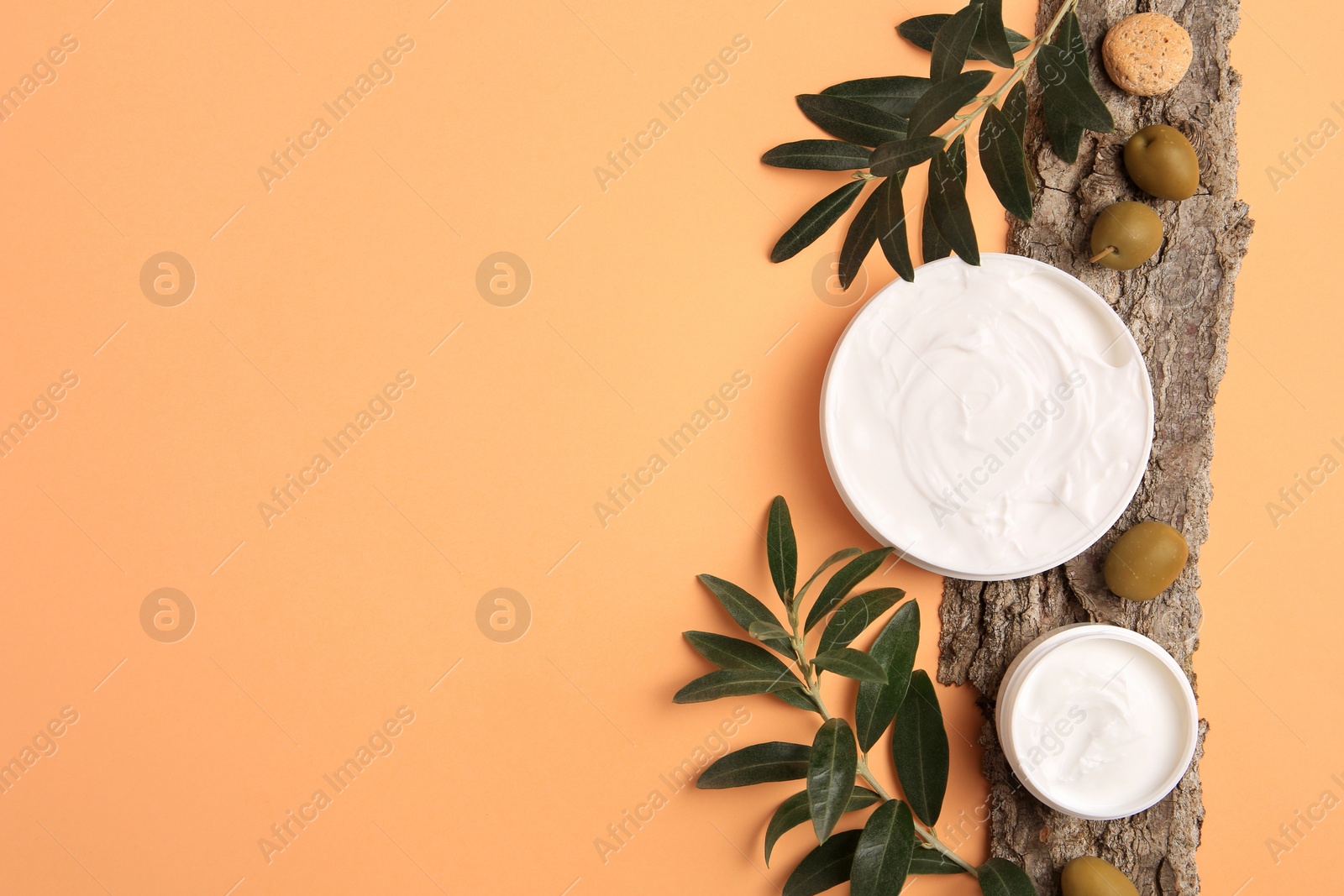 Photo of Flat lay composition with jars of cream and olives on pale orange background. Space for text