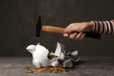 Woman breaking piggy bank with hammer on table