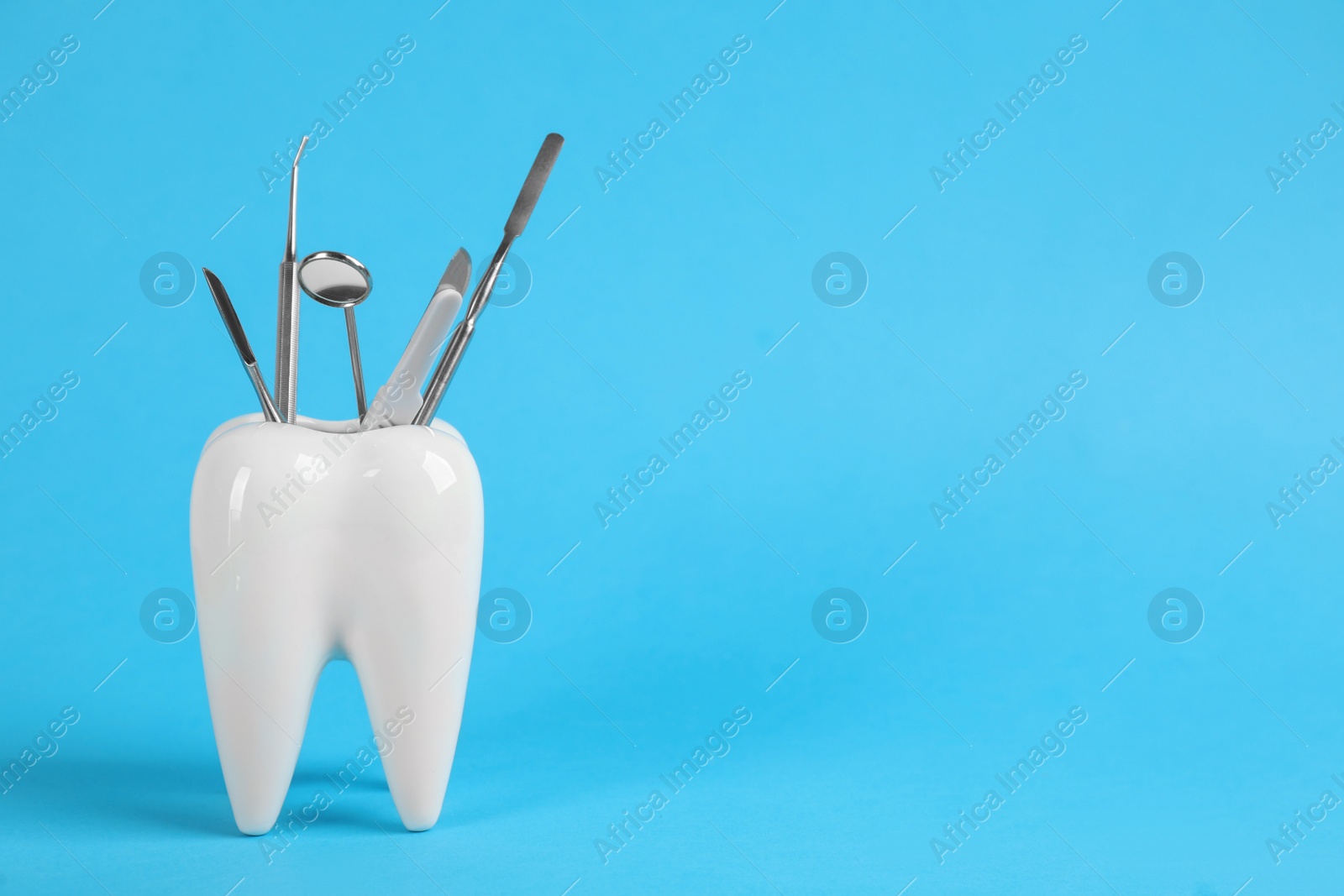 Photo of Tooth shaped holder with dentist's tools on light blue background. Space for text