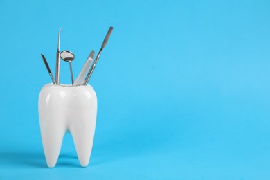 Tooth shaped holder with dentist's tools on light blue background. Space for text