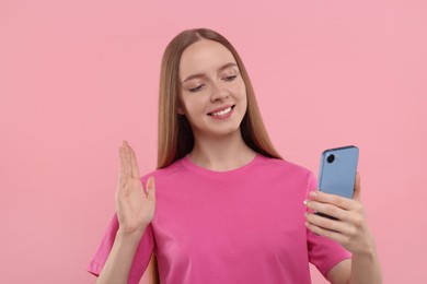 Photo of Happy young woman using smartphone and having video chat on pink background