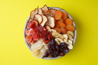 Photo of Wicker basket with different dried fruits on yellow background, top view