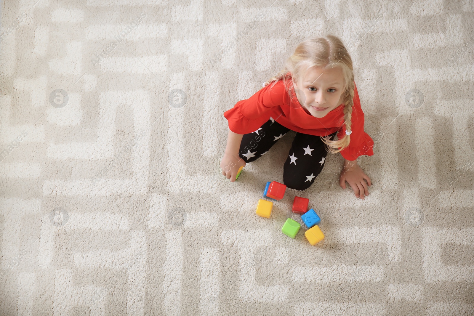 Photo of Cute little girl sitting on cozy carpet with cubes at home