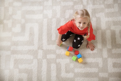 Cute little girl sitting on cozy carpet with cubes at home