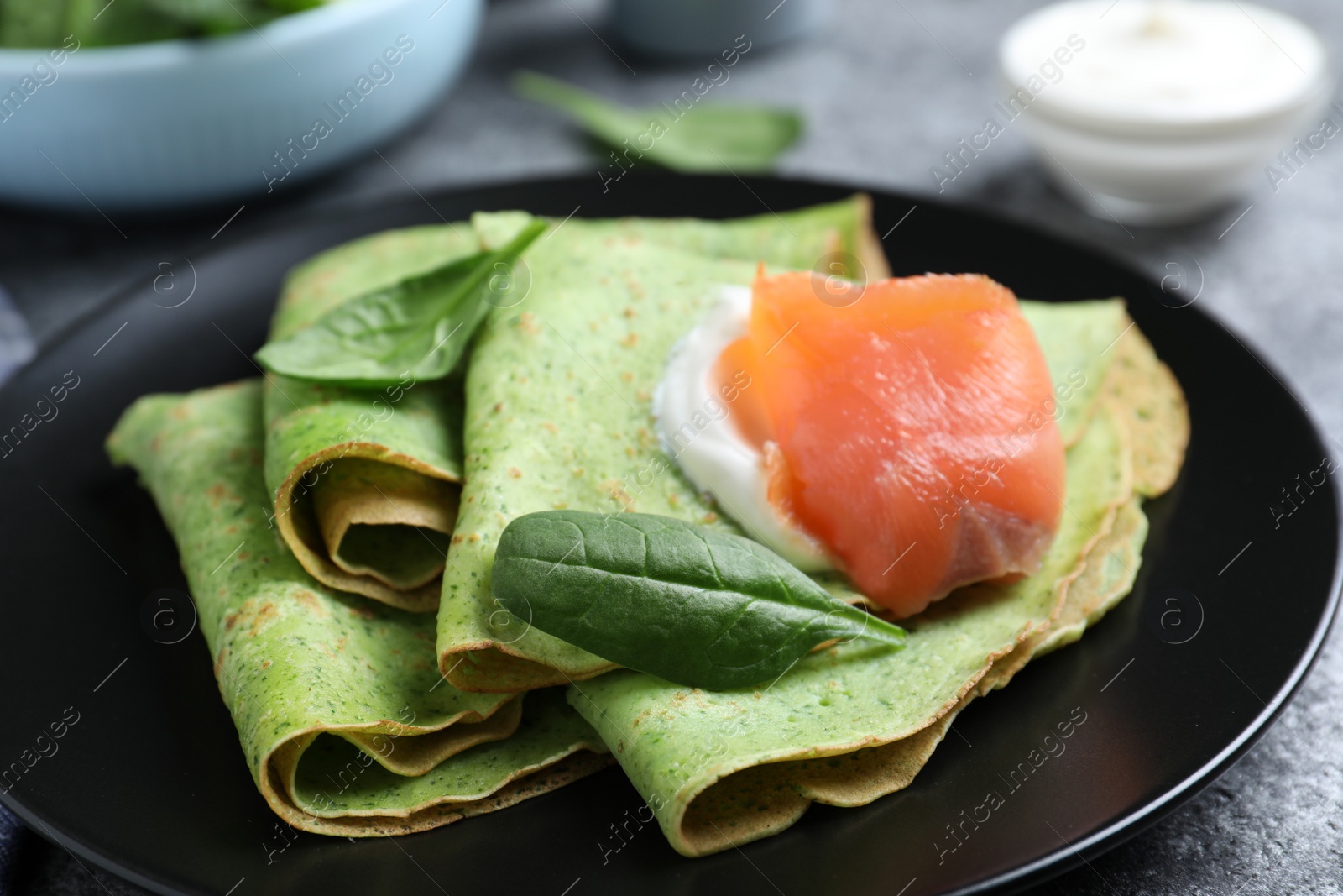 Photo of Delicious spinach crepes with salmon and cream on table, closeup