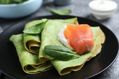 Delicious spinach crepes with salmon and cream on table, closeup