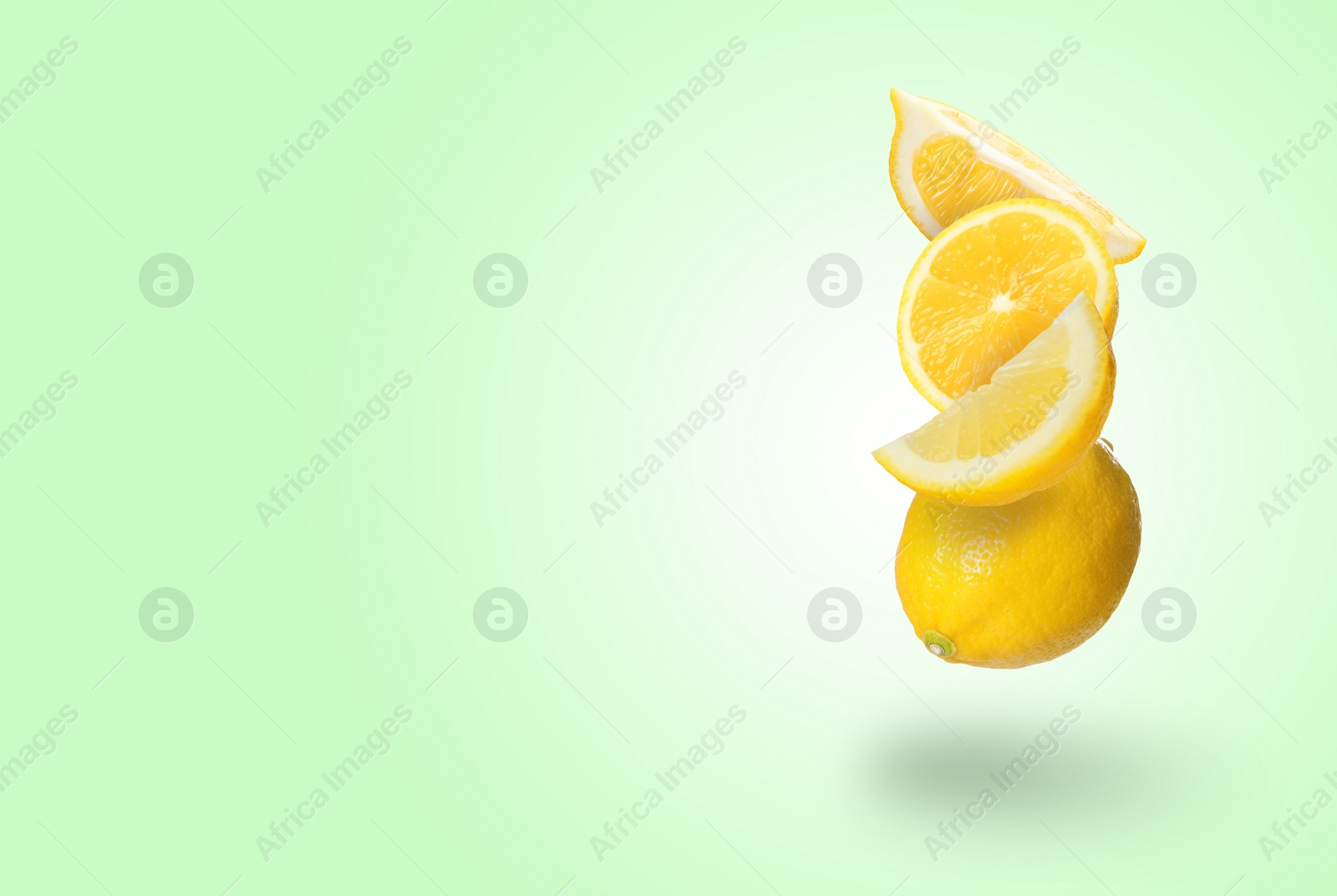 Image of Cut and whole fresh lemons falling on light green background, space for text