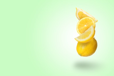 Image of Cut and whole fresh lemons falling on light green background, space for text