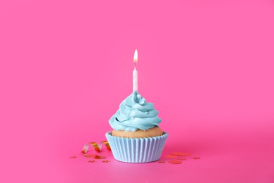 Photo of Delicious birthday cupcake with burning candle, streamer and confetti on pink background