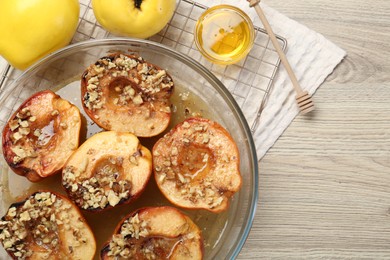 Delicious baked quinces with nuts in bowl, honey and fresh fruits on wooden table, flat lay. Space for text