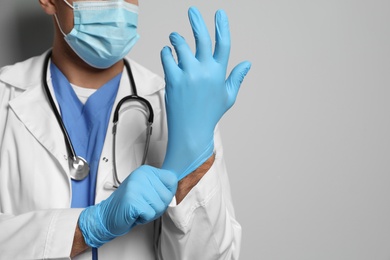 Photo of Doctor in protective mask putting on medical gloves against light grey background, closeup. Space for text