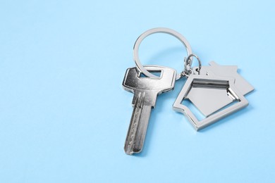 Photo of Key with keychain in shape of house on light blue background, closeup. Space for text
